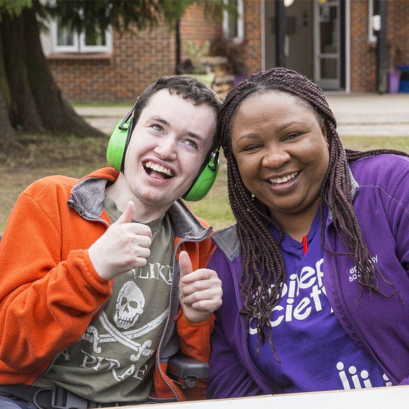 Resident and support worker enjoying a summer party at the Epilepsy Society. Both are smiling at the camera.