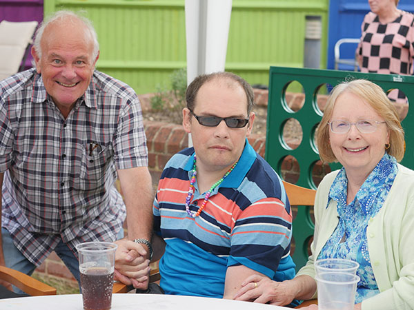 Chris and Marilyn are enjoying a drink outside in the garden with son, Daniel. Daniel is wearing a stripey t-shirt and sunglasses